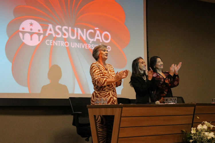 Professoras na mesa solene aplaudindo os formandos
