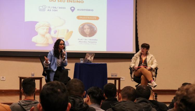 Professora Natália Mendes Teixeira fala ao público no auditório do Centro Universitário Assunção, com projeção de slide ao fundo contendo o título da palestra.